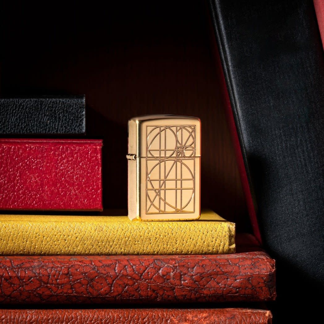 Golden Ratio ArmorÂ® High Polish Brass Windproof Lighter standing on books