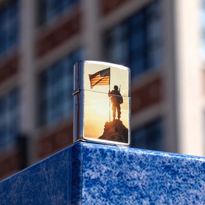 Lifestyle image of Zippo Soldier and Flag Design Brushed Chrome Windproof Lighter standing on the corner of a bright blue stone wall, showing the front and hinge side of the lighter with a blurred building as the background. 

