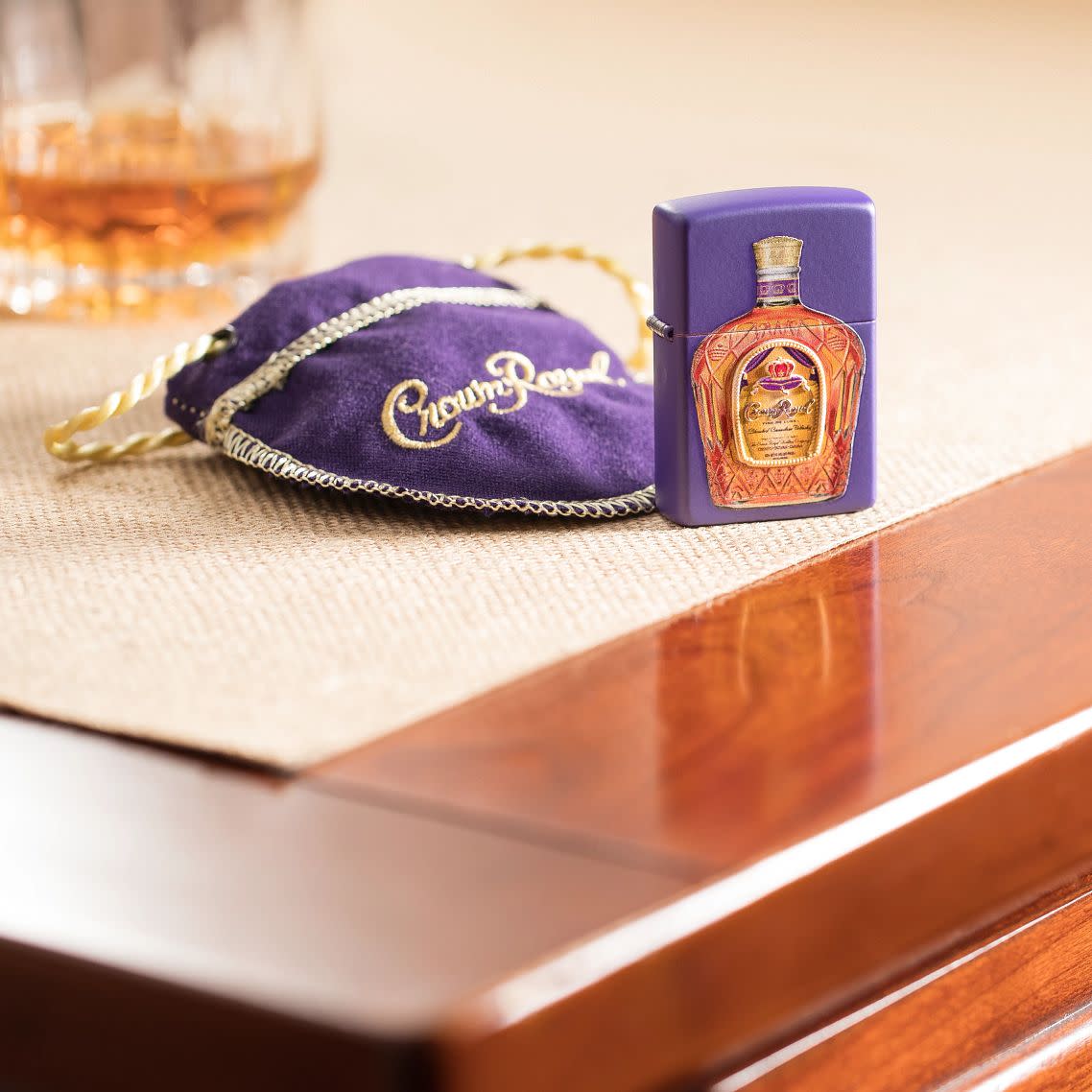 Lifestyle image Crown RoyalÂ® Purple Matte Windproof Lighter and Crown RoyalÂ® Pouch on a side stand with a drink.